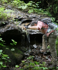 erschöpfter Wanderer erfrischt sich am Quellwasser im Nationalpark Bayerischer Wald in der Nähe der Ferienwohnung FeWo Moosau in D-94258 Frauenau © Gine Selle, Frauenau